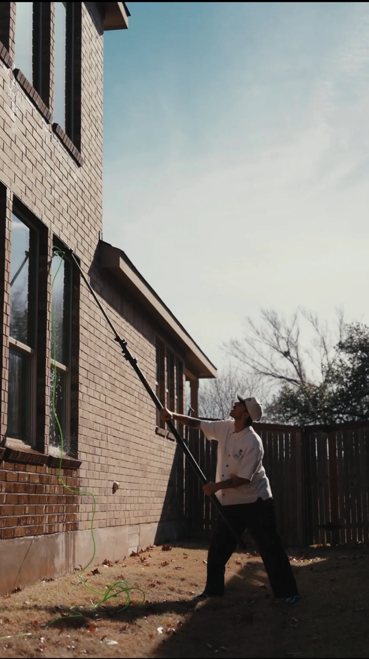 Crew member cleaning high exterior windows on a brick property with a long pole